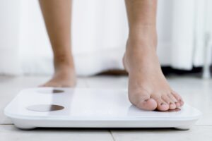 Closeup of a woman’s feet with painted toenails stepping on a scale to measure her weight.