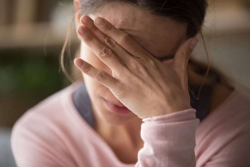A close-up image of a woman holding her hand to her forehead in pain.