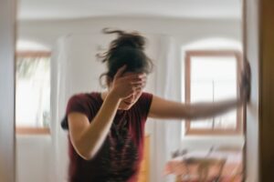 A woman leaning against a wall, holding her forehead as she experiences vertigo.