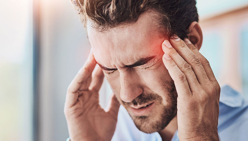 A man presses his fingers to his temples. His eyes are closed, and he appears to be in pain.