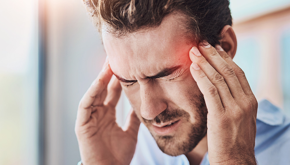 A man presses both hands to his temples. His eyes are closed and he appears to be in pain.