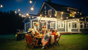 A family enjoying dinner outdoors in the backyard with a blue house in the background.
