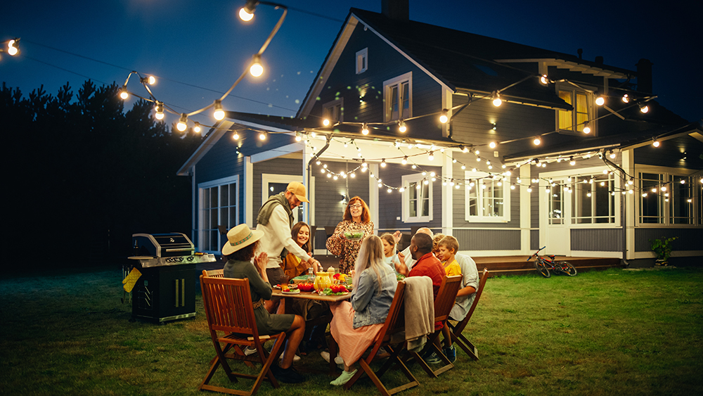 A family enjoying dinner outdoors in the backyard with a blue house in the background.