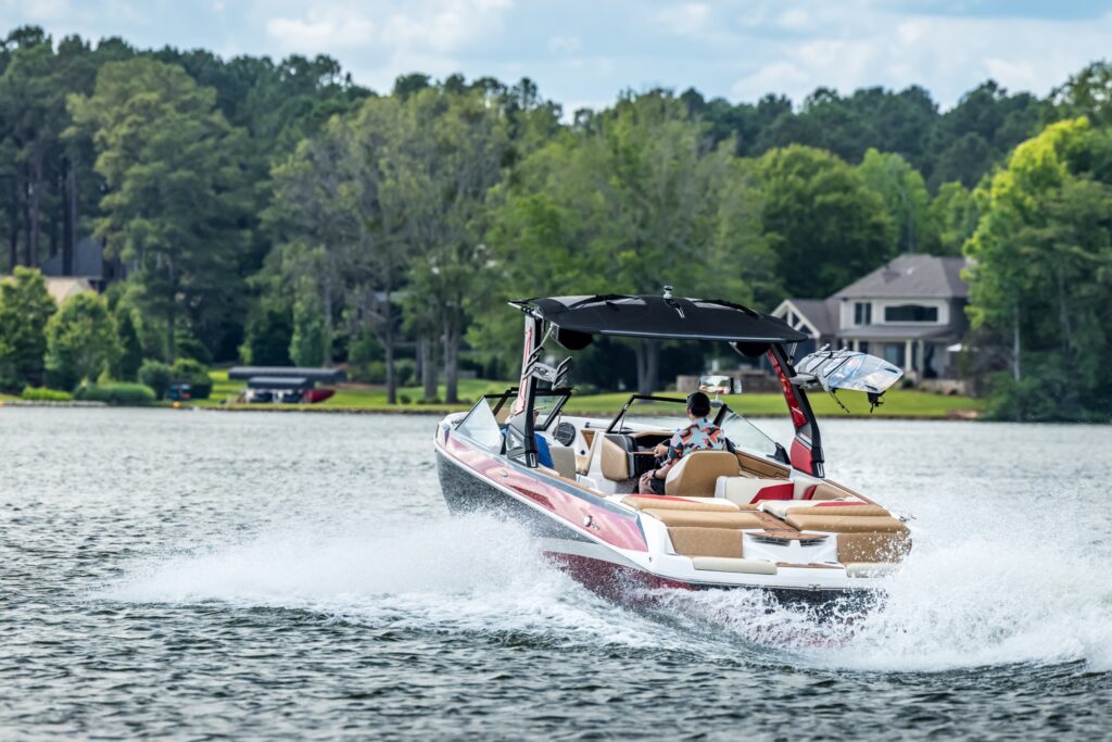 A man driving a power boat on a lake with trees and homes in the background.