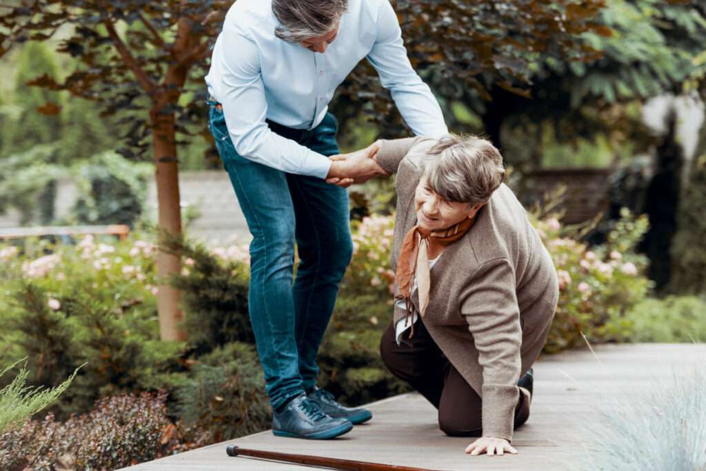 Man helping elderly woman up after a fall outdoors