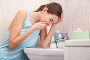 Young woman leaning over bathroom sink appearing ill or nauseous