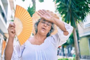 Middle-aged woman with grey hair using a handheld fan to cool herself during a heat wave